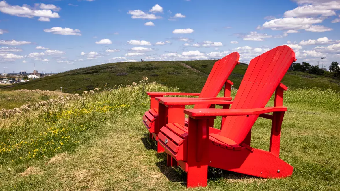 Two red Adirondack chairs on a green grass at Downsview Park.