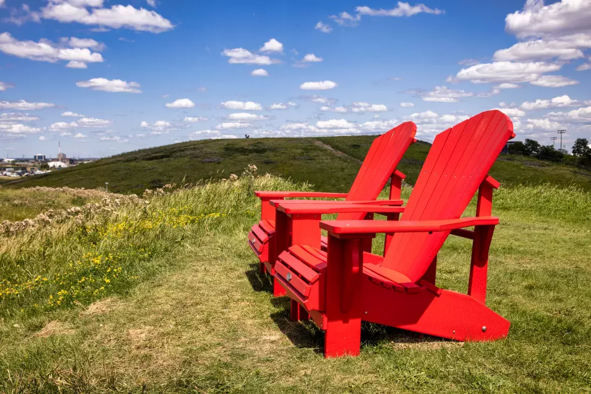 Two red Adirondack chairs on a green grass at Downsview Park.